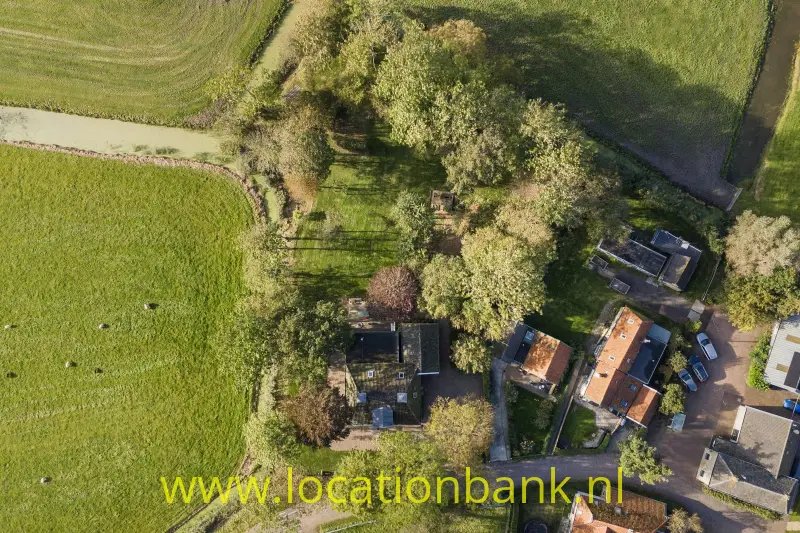 Meerdere huizen liggen tussen bomen, omgeven door groene velden en smalle landwegen.