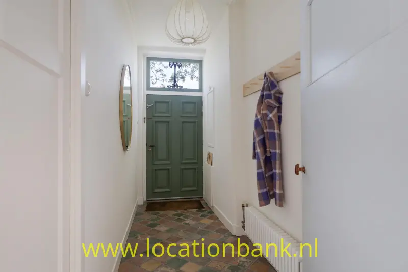 Groene deur aan het einde van een smalle hal met kleurrijke patroontegels en een radiator.
