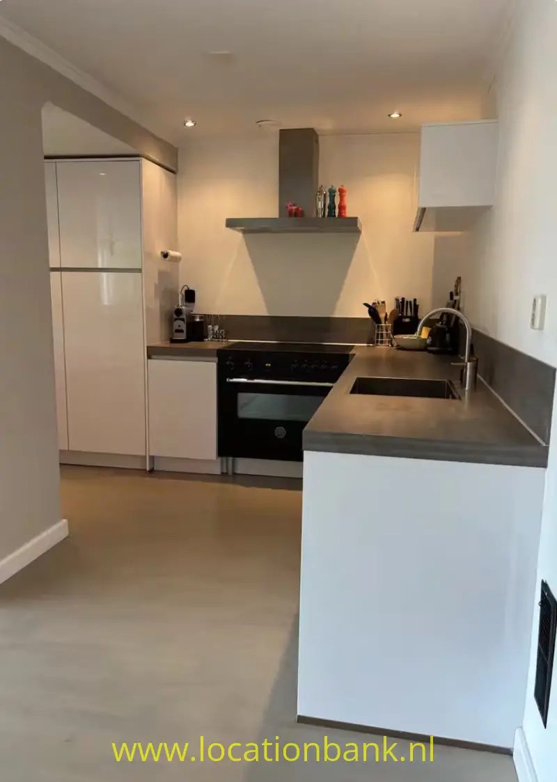 Moderne keuken met kookeiland, ingebouwde oven, inductiekookplaat, spoelbak en witte keukenkasten.