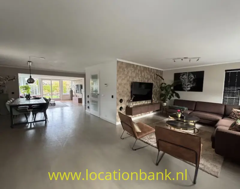 Open woonruimte met een eethoek bij de ramen en een zithoek met televisie.