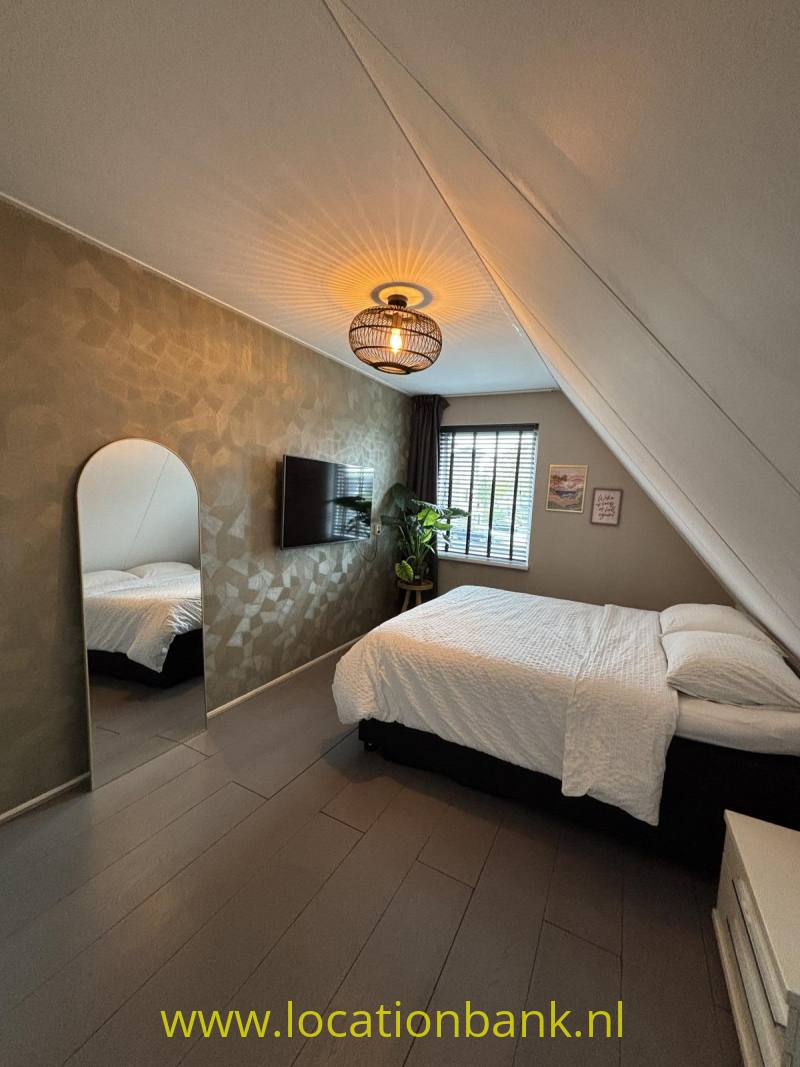 Slaapkamer met twee eenpersoonsbedden met wit beddengoed, een schuin plafond, een raam met jaloezieën en een hanglamp.