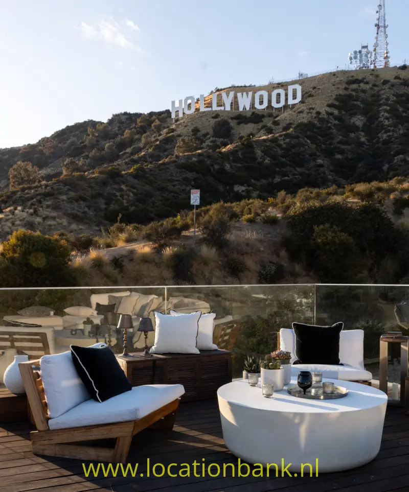 Het Hollywood-bord staat op een met struikgewas bedekte heuvel achter een terras met stoelen en een ronde tafel.