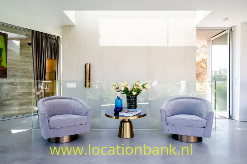 Twee paarse fauteuils staan naast een ronde tafel met bloemen in een lichte hal.
