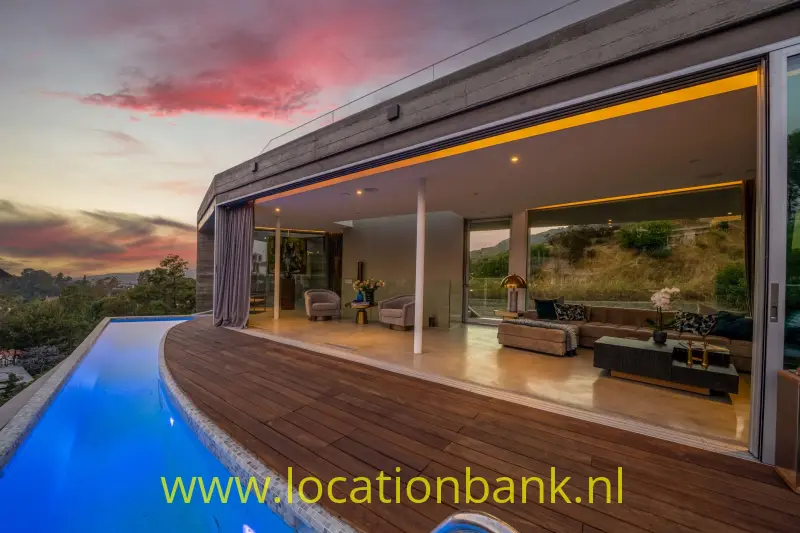 Woning met een overdekt terras, een verlicht zwembad en uitzicht op Hollywood Hills bij zonsondergang.