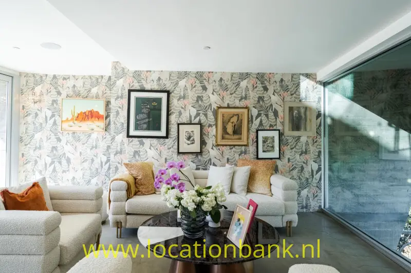 Woonkamer met botanisch behang, twee lichte banken, een ronde salontafel en ingelijste kunst aan de muur.