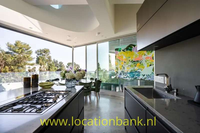 Keuken met een kookeiland met gasfornuis, hoge ramen en een kleurrijk abstract schilderij.
