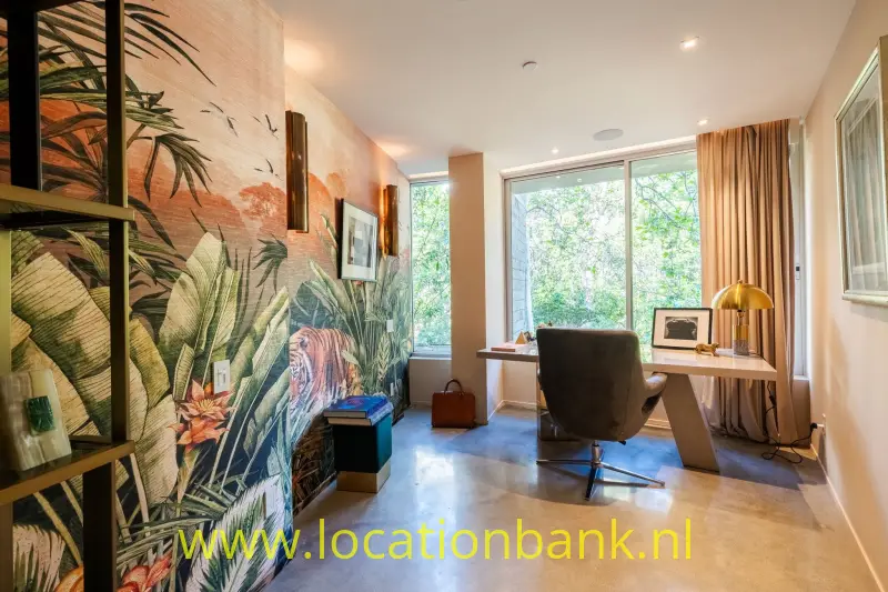 Werkruimte met een bureau voor hoge ramen en een botanische muurschildering.
