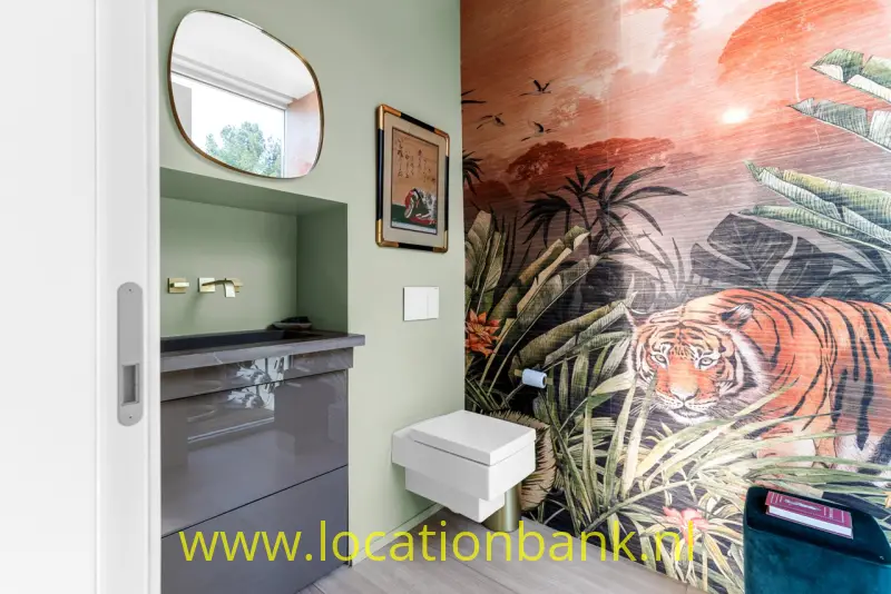 Badkamer met tijger- en junglebehang, een zwevend wit toilet, een donker wastafelmeubel en groene wanden.