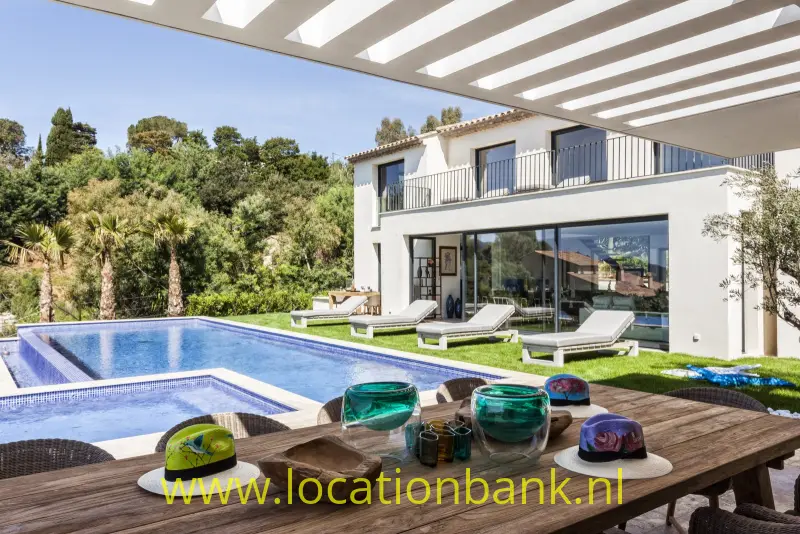 Witte woning met balkon, zwembad en overdekt terras, omgeven door groene beplanting.