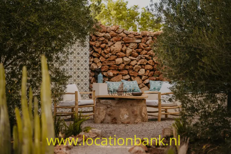 Buitenzitplek met houten stoelen, een lage stenen tafel, een stenen muur en een betegelde achterwand.