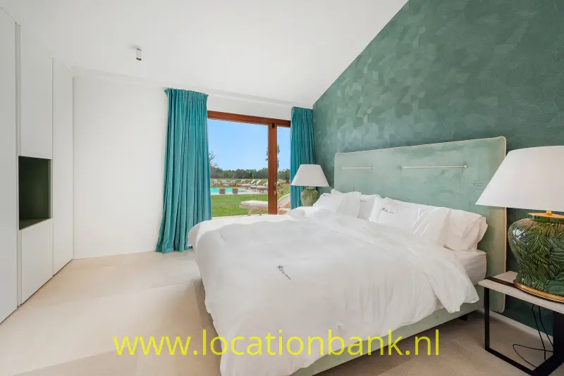 Slaapkamer met een opgemaakt tweepersoonsbed, een groen getextureerde wand en turquoise gordijnen naast het raam.