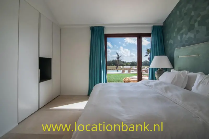 Slaapkamer met een opgemaakt bed, een groene wand met patroon en een raam met turquoise gordijnen.