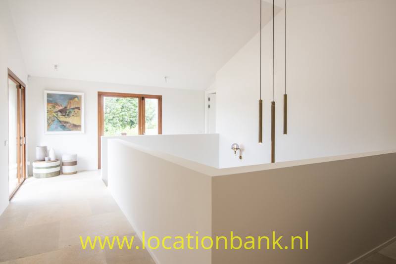 Witte binnenruimte met een lage scheidingswand, drie hanglampen en houten raamkozijnen.