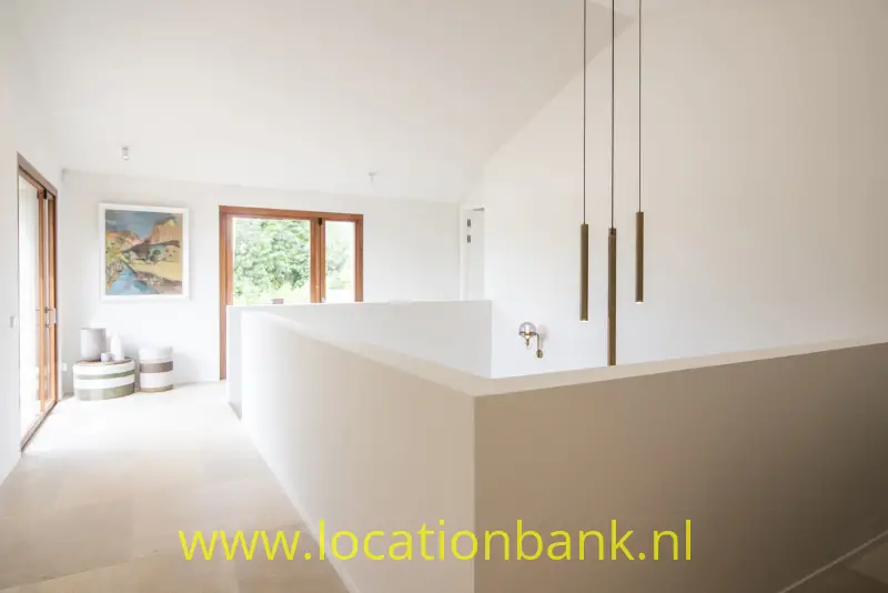 Witte binnenruimte met een lage scheidingswand, drie hanglampen en houten raamkozijnen.