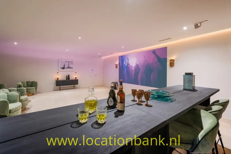 Donkere eettafel met glazen en flessen, omringd door stoelen en een kleurrijk kunstwerk aan de wand.