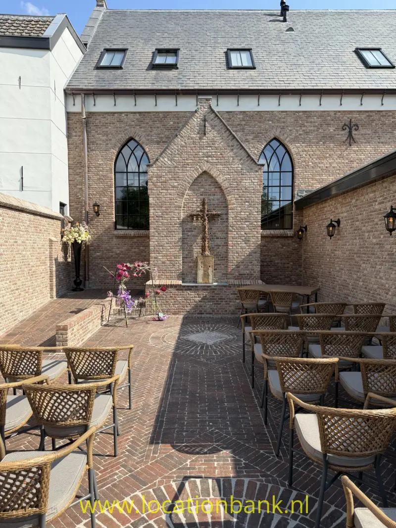 Bakstenen binnenplaats met gevlochten terrasstoelen, spitsboogvensters en een centrale stenen nis.