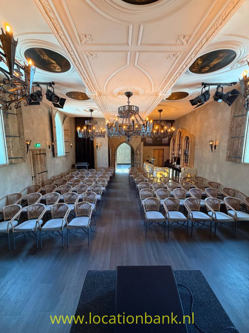 Interieur met rijen gevlochten stoelen, kroonluchters en een gedecoreerd plafond met ronde schilderingen.
