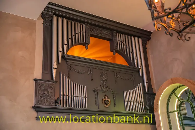 Een orgel met metalen pijpen, houtsnijwerk, een boogvormige opening en een kroonluchter erboven.