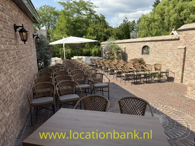 Bestrate binnenplaats met rijen gevlochten stoelen, houten tafels, parasols en omliggende bakstenen muren.