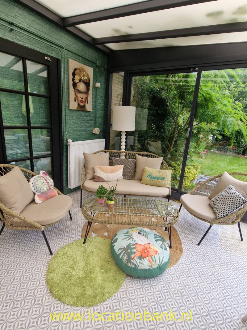 Zitgedeelte met een beige bank, twee fauteuils, een glazen wand en zicht op een groene tuin.