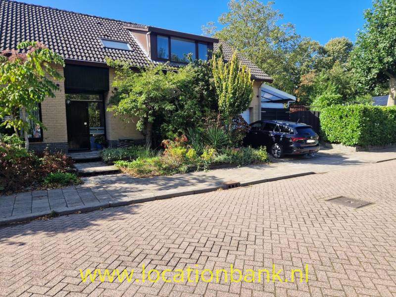 Bakstenen woonhuis met aangebouwde garage, voortuin en zwarte auto aan een met klinkers bestrate straat.