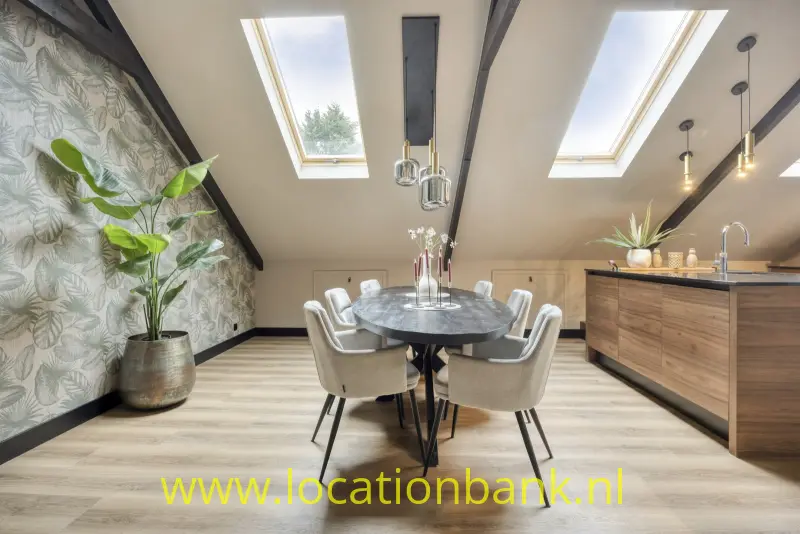 Ovale eettafel met vier stoelen in een lichte keuken met twee dakramen en een houten kookeiland.