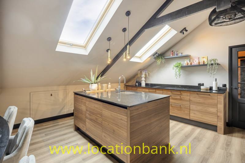 Keuken met een centraal keukeneiland, houten kasten, donkere werkbladen en dakramen in het schuine plafond.
