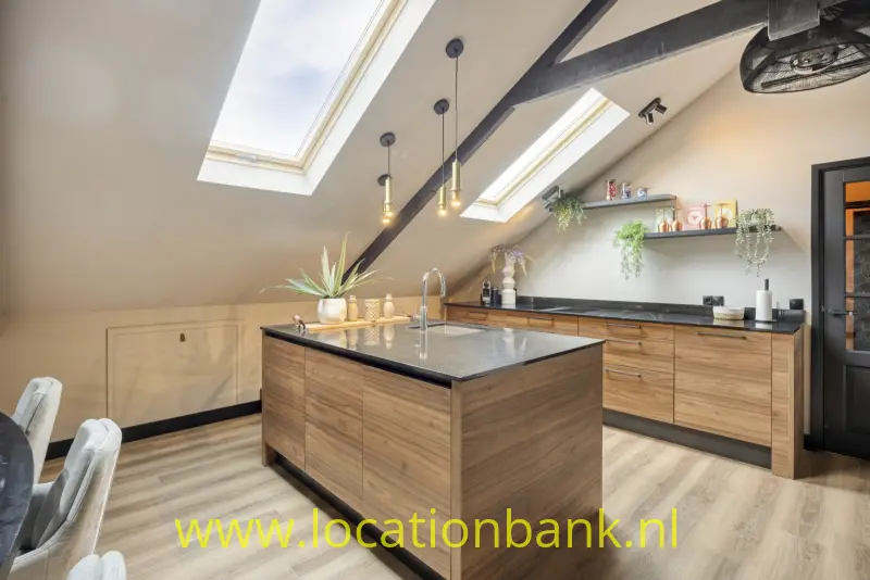 Keuken met een centraal keukeneiland, houten kasten, donkere werkbladen en dakramen in het schuine plafond.