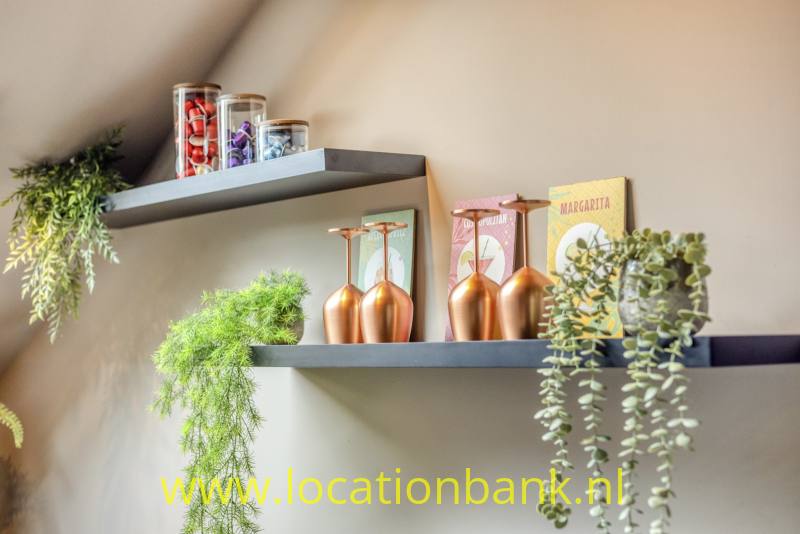 Donkere wandplanken combineren hangplanten met glazen potten en koperkleurige decoratieve objecten.