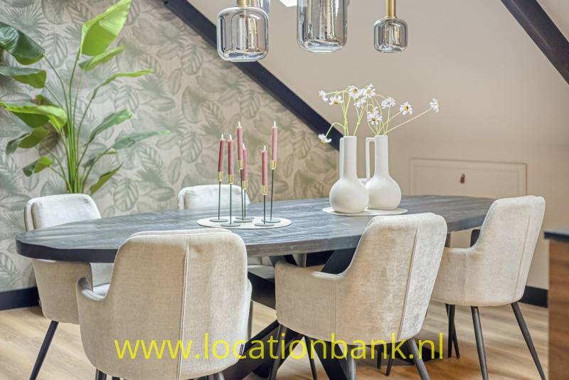 Donkere eettafel met gestoffeerde stoelen, hanglampen, twee witte vazen en botanisch behang.