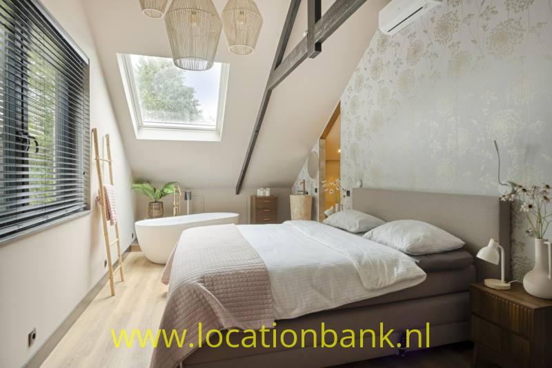 Slaapkamer met een tweepersoonsbed, een schuin dak, een dakraam en een vrijstaand bad.