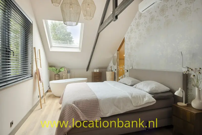 Slaapkamer met een tweepersoonsbed, een schuin dak, een dakraam en een vrijstaand bad.