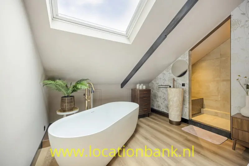 Vrijstaand wit bad onder een dakraam in een badkamer met een vloer in houtlook en een inloopdouche.