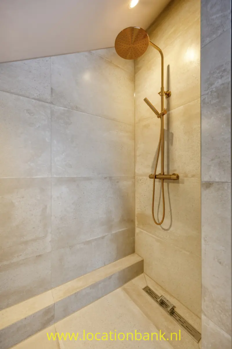 Douche met een ronde regendouche, handdouche en lineaire afvoer tussen grote lichtgekleurde tegels.