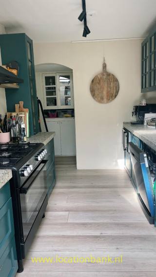 Küche mit dunkelgrünen Schränken, einem runden Holzbrett an der Wand und einem hellen Boden in Holzoptik.