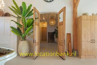 Offene hölzerne Doppeltüren geben den Blick auf einen hellen Flur mit großer Zimmerpflanze, Holzschrank und Pendelleuchte frei.