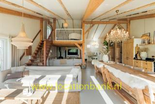 Grosse Wohnzimmer mit sichtbaren Holzbalken, einer Treppe zu einer Galerie und einem langen Esstisch.