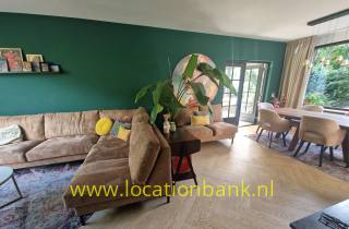 Wohnzimmer mit einer grünen Wand, Ecksofa, Pflanzen, Esstisch und Glastüren.