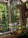 Tall windows with metal muntins show greenery outside beside potted plants and woven baskets in a wooden room.