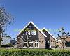 Brick house with a dark wooden gable, pitched roof, pruned trees and a hedge.