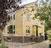 Gelbes Backsteinhaus mit dunklem Sockel, weißen Fensterrahmen und überdachtem Eingang neben einer Treppe.