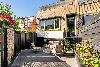 Gepflasterte Terrasse mit Sitzbereich, blühenden Pflanzen, einer Backsteinfassade und Stufen.