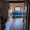 Ein blaugrünes Sofa steht an einer Holzwand unter einem Fenster, sichtbar durch eine offene Tür.