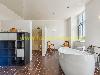 Eine freistehende weiße Badewanne steht in einem hellen Badezimmer mit großen Fenstern und einem dunklen Holzboden.