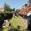Ein Backsteingebäude mit rotem Ziegeldach grenzt an einen schmalen Rasenstreifen zwischen Gärten.