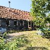 Dunkles Holzhaus mit einem roten Ziegeldach, Schornstein, Terrasse und Garten.