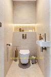 Beigefarbenes Badezimmer mit einer Toilette, einem Waschbecken, goldfarbenen Armaturen und einer Nische mit indirekter Beleuchtung.
