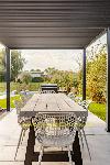 Überdachte Garten Terrasse mit langem Holzesstisch und geflochtenen Stühlen, umgeben von einem grünen Garten.