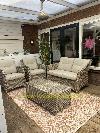 Sitzbereich mit zwei Rattansesseln, einem Rattansofa, einem niedrigen Tisch und einem gemusterten Teppich.