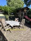 Ein hölzernes Spielhaus mit roter Rutsche steht hinter einem Gartentisch mit weißer Tischdecke auf einer gepflasterten Terrasse.